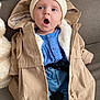 baby, coat, hat, blue_shirt, jeans, sitting, couch, plush_toy, surprised_expression, knit_booties, child, indoor, warm_clothing, cute, person, face, headwear, buttoned_shirt, casual_wear, soft_fabric
