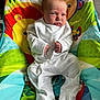 baby, infant, onesie, baby_chair, colorful, animal_print, face, expression, indoor, furniture, seated, clothing, hands, feet, young_child, child, person, cute, portrait, baby_toys