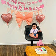 Jind is registered to the contest to win money with this photo: baby, child, birthday, cake, chair, balloons, pink, banner, bow, celebration, indoor, flooring, table, wall, person, young_child, decorations, party, festive, cute