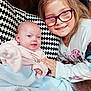 Matilda is registered to the contest to win money with this photo: baby, child, glasses, blanket, smile, sibling, cushion, pattern, cozy, indoor, happy, portrait, clothing, face, hand, toddler, young_girl, couch, family, together