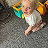 blonde_hair, blue_eyes, carpet, child, childhood, colorful_toys, curly_hair, floor, happy, home, indoor, kneeling, pants, person, playtime, smiling, toddler, toy, white_shirt, young_child