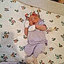 adult_face_partial, baby, baby_girl, bedroom, blanket, cozy, floral_pattern, headband, indoor, infant, mittens, mouth_open, newborn, pacifier, peaceful, portrait, purple_outfit, sleeping, socks, soft_texture
