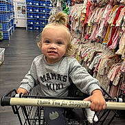 River joined the competition — help win amazing prizes! toddler, child, shopping_cart, store, clothing, baby_clothes, sweatshirt, smiling, indoor, aisle, pony_tail, flooring, retail, shopping, person, happy, casual_wear, socks, handle, colorful