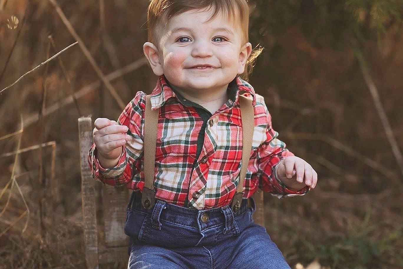 Junior is registered to the contest to win money with this photo: baby_toddler_clothing, clothing, face, finger, flash_photography, grass, hand, happy, head, joy, leaf, people_in_nature, person, plaid, plant, red, skin, sleeve, smile, tartan