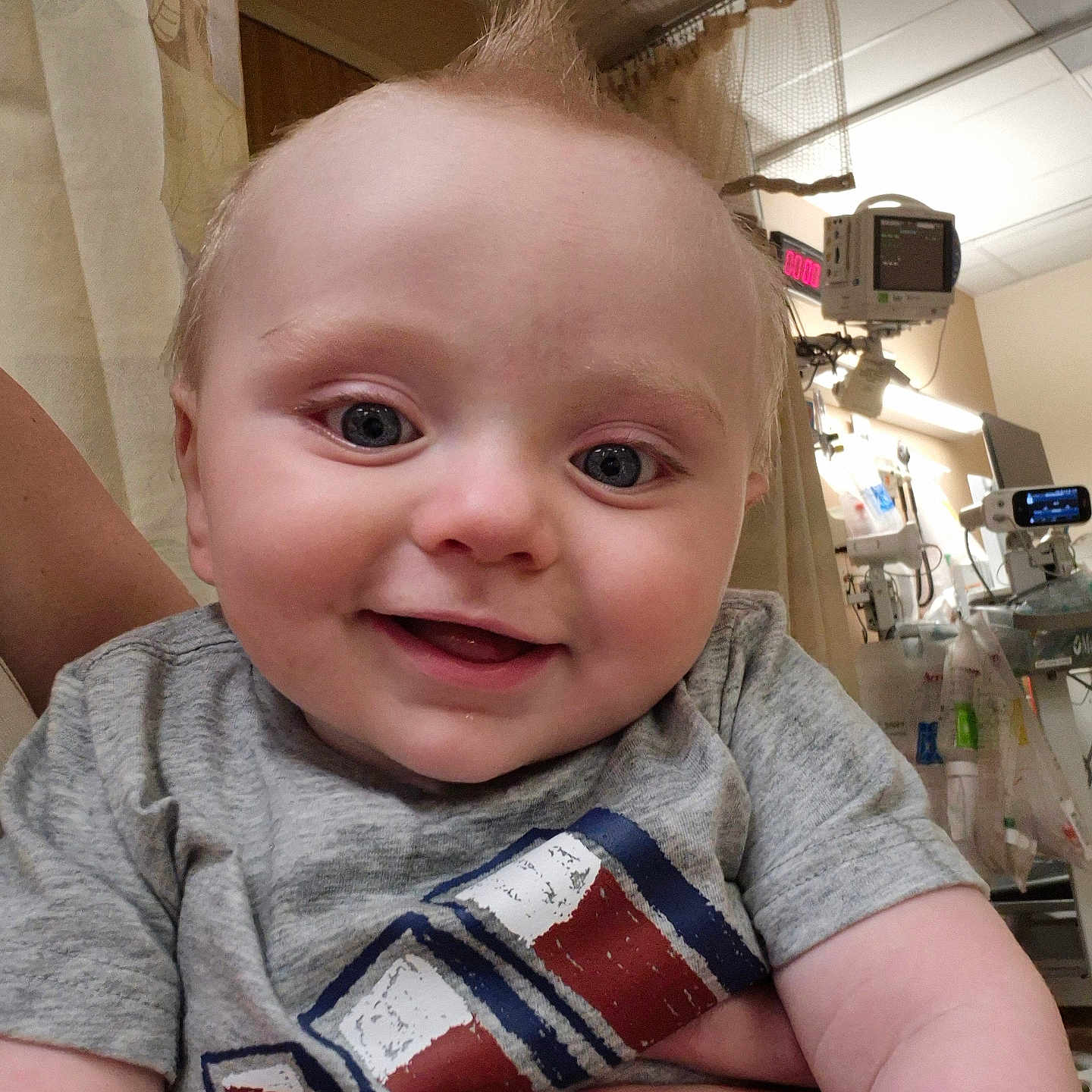 Hunter is registered to the contest to win money with this photo: baby, child, closeup, curtain, face, hand, happy, holding, hospital, indoor, infant, light, medical_equipment, mohaawk, monitor, person, skin, smile, tshirt, wall