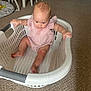 baby, child, laundry_basket, pink_clothing, carpet, indoor, floor, furniture, playmat, hand, foot, curious, sitting, home, person, infant, looking_down, grip, white, plastic