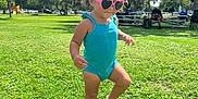 Arianna joined the competition — help win amazing prizes! child, toddler, sunglasses, pink_bow, blue_romper, grass, park, sunny, trees, people, bench, shoes, sandals, shadow, outdoor, playground, daylight, cute, walking, nature