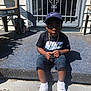child, boy, nike, cap, tshirt, chain, sneakers, white_shoes, sitting, doorstep, shadow, outdoor, concrete, plastic_chair, metal_door, carpet, sunlight, serious_expression, person, casual_clothing