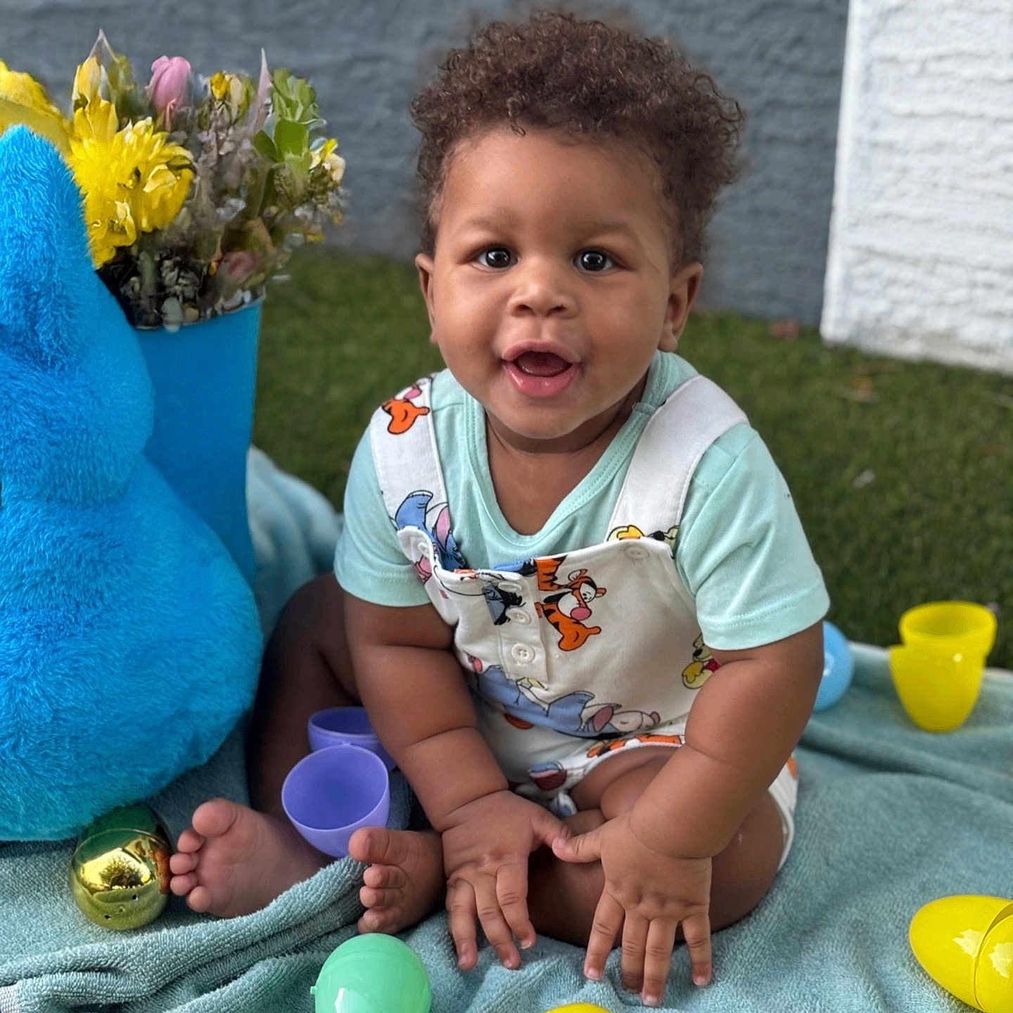 Zyaire is registered to the contest to win money with this photo: toddler, child, baby, smiling, curly_hair, plastic_eggs, blue_towel, stuffed_toy, outdoor, grass, flowers, playtime, happy, sitting, colorful, toy, cute, summer, daylight, casual_clothing