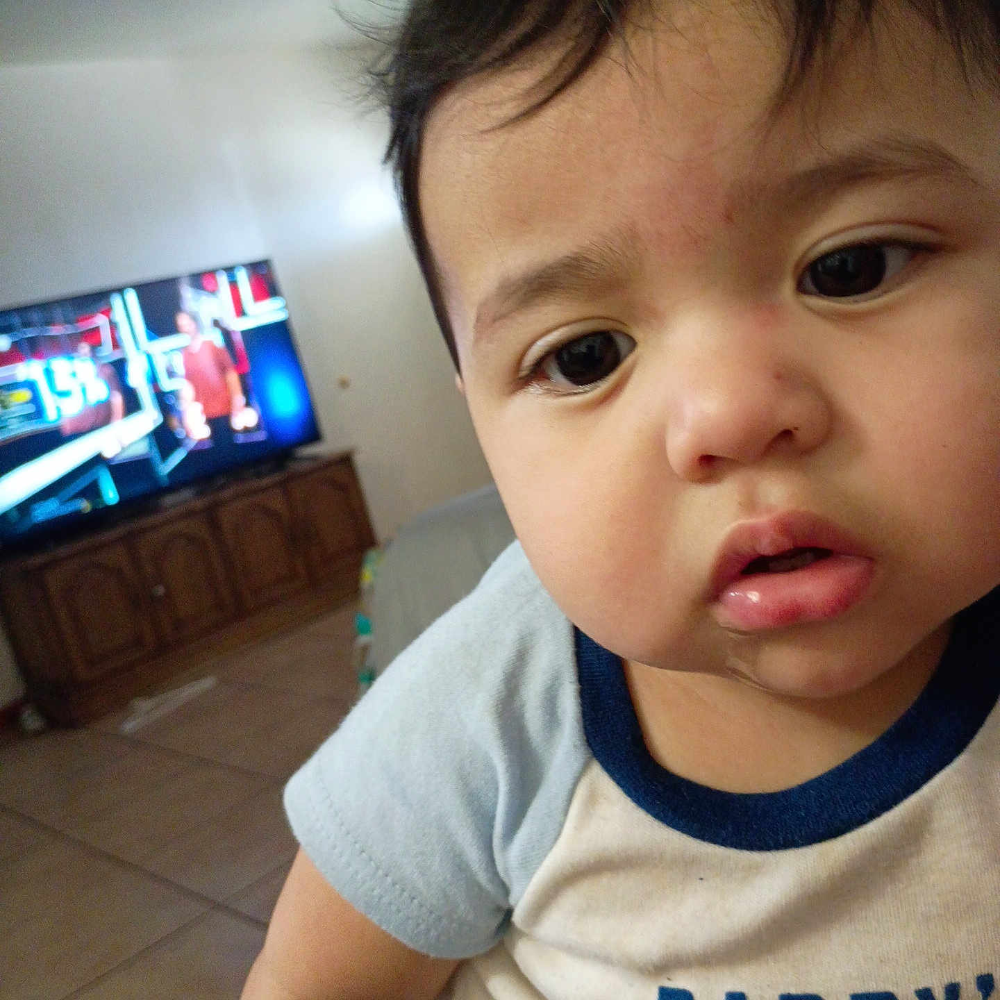 Andres joined the competition — help win amazing prizes! baby, child, infant, portrait, close_up, face, eyes, expression, curious, indoor, living_room, television, cabinet, furniture, shirt, clothing, short_sleeves, sitting, home, photography