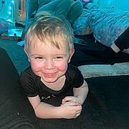 Maverick is registered to the contest to win money with this photo: toddler, child, smiling, indoor, person, carpet, couch, clothing, hand, face, hair, black_shirt, blue_light, relaxing, home, floor, furniture, sitting, adult, legs