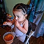 Amy is registered to the contest to win money with this photo: toddler, child, high_chair, braided_hair, rice, plastic_container, spoon, eating, table, curtain, indoor, flooring, snacks, food, person, clothing, hair, seat, home, meal