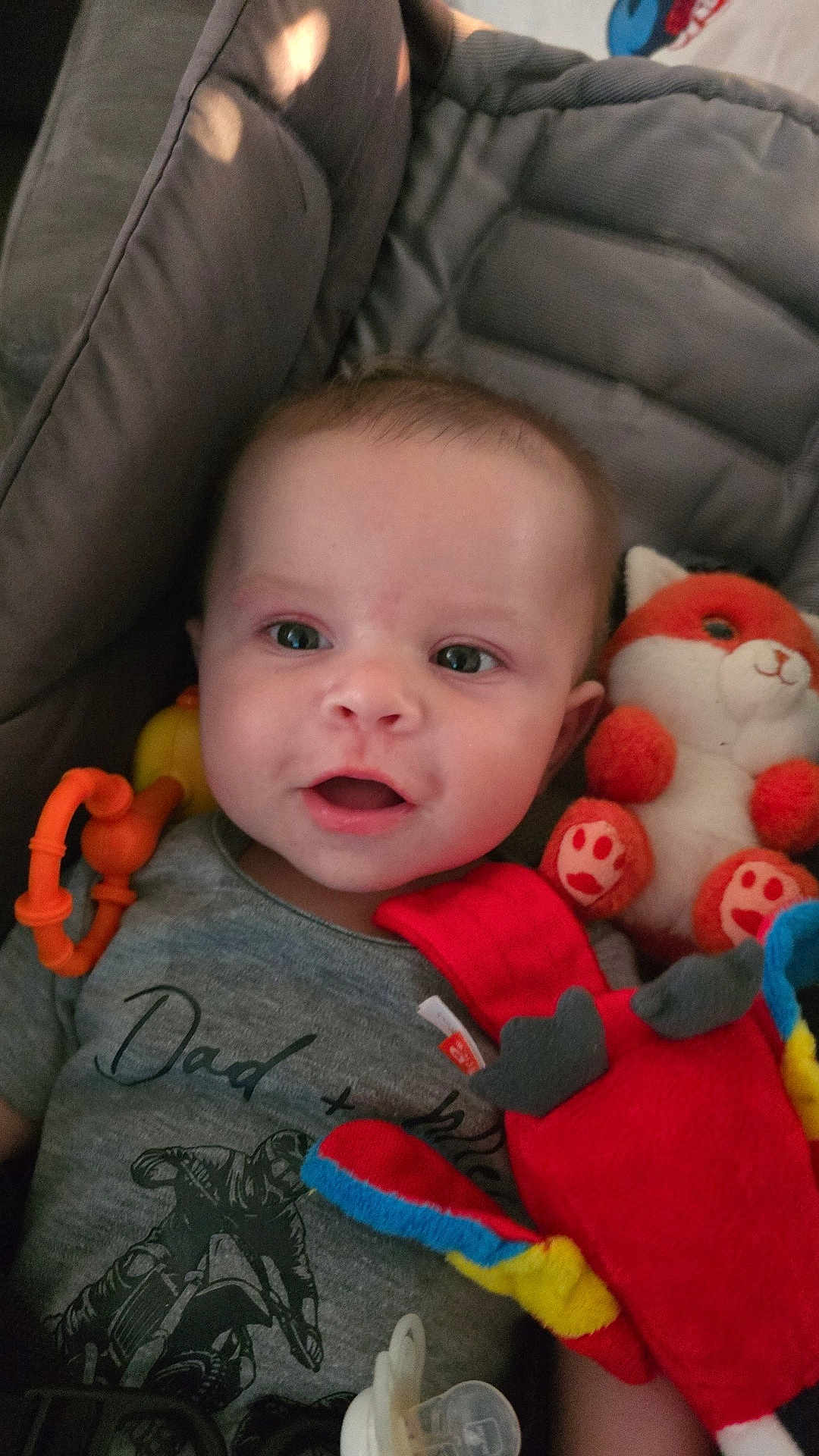 Mayron a rejoint le concours — aidez-le/la à gagner de superbes lots ! baby, infant, smiling, face, eyes, plush_toy, fox_toy, red_toy, pacifier, clothing, shirt, motorcycle_print, text_on_clothing, baby_toys, soft_toys, child, closeup, indoor, cushion, happy