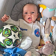 Mayron a rejoint le concours — aidez-le/la à gagner de superbes lots ! baby, infant, plush_toy, soccer_ball, onesie, bassinet, pacifier, soft_toys, child, cute, surprised_expression, person, indoor, baby_clothes, stuffed_animal, toy, smiling, small_child, sleeping_area, comfort