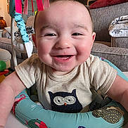 Jack is registered to the contest to win money with this photo: baby, infant, smiling, play_seat, onesie, owl_applique, living_room, couch, blanket, toy, ribbons, rosy_cheeks, close_up, portrait, happy, sitting, arm, drool, colorful, adorable