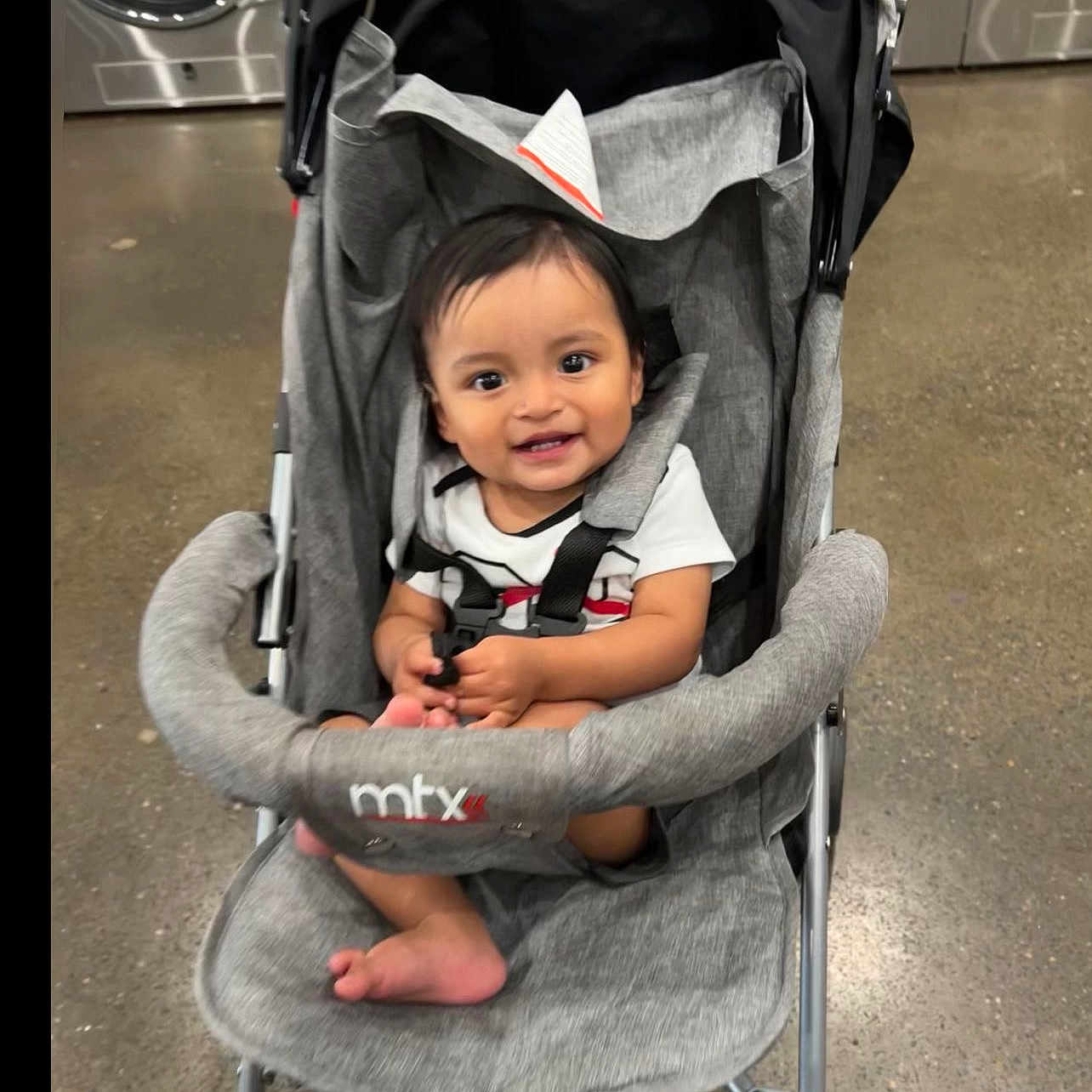 Jonnathan joined the competition — help win amazing prizes! baby, baby_clothes, black_hair, child, clothing, fabric, floor, footwear, handlebar, happy, indoor, infant, laundromat, person, seat, smiling, stroller, toddler, toy, washing_machine