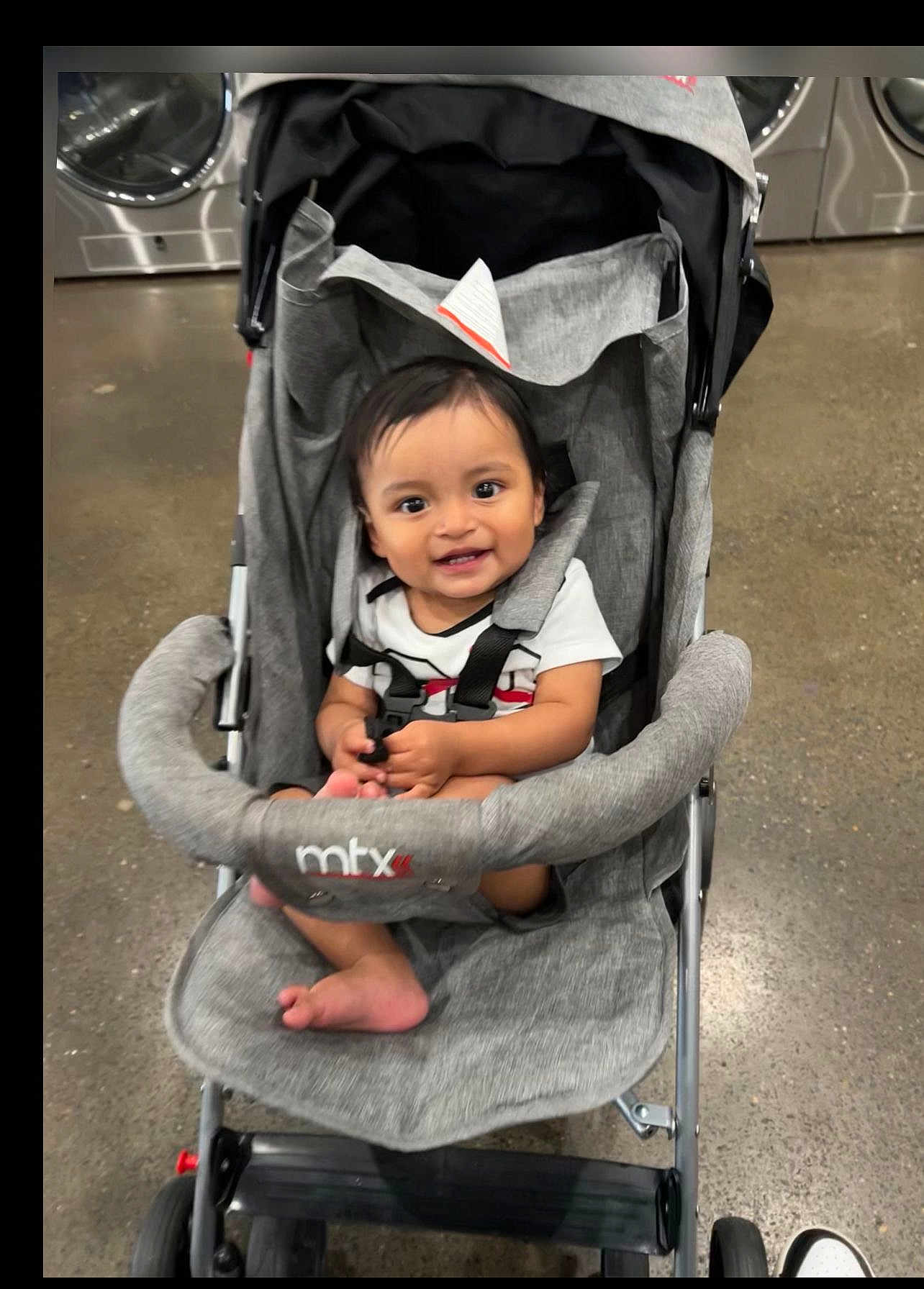 Jonnathan joined the competition — help win amazing prizes! baby, stroller, smiling, indoor, laundromat, washing_machine, clothing, footwear, floor, seat, baby_clothes, happy, child, infant, person, toddler, toy, handlebar, fabric, black_hair