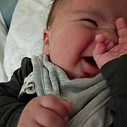 Xavier is registered to the contest to win money with this photo: baby, infant, smile, hand, face, scarf, clothing, close_up, happy, cute, child, portrait, indoors, soft_light, cozy, person, skin, expression, fingers, playful