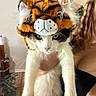 animal, black_and_white, cat, costume, cute, ears, expression, face, fur, hair, hand, holding, home, indoor, person, pet, rug, tiger_hat, wall, white_cat
