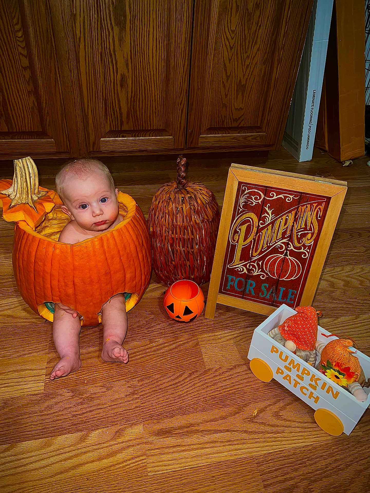 Carson joined the competition — help win amazing prizes! baby, infant, pumpkin, hollowed_pumpkin, halloween, jack_o_lantern, wooden_floor, kitchen_cabinet, seasonal_decor, sign, for_sale_sign, decorative_basket, toy_wagon, barefoot, cute, portrait, indoor, holiday, orange, costume_prop