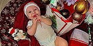 Carson joined the competition — help win amazing prizes! baby, infant, christmas, christmas_tree, ornament, candy_cane, stocking, santa_hat, smile, festive, gift_bag, tree_skirt, red, white, plush_toy, baby_clothes, hardwood_floor, holiday_card, celebration, feet