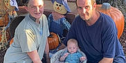 Kenny is registered to the contest to win money with this photo: family, baby, adult, tree, pumpkin, scarecrow, blanket, outdoor, grass, autumn, fall, basket, smile, tattoo, blue_clothing, green_gourd, sunlight, nature, people, happy