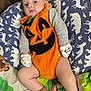 baby, infant, pumpkin_costume, orange_clothing, mittens, socks, pillow, blanket, cute, child, indoors, pattern, animal_print, soft_toys, comfort, couch, face, person, resting, portrait