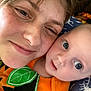 adult, baby, face, smile, closeup, portrait, orange_clothing, green_leaf, blanket, animal_pattern, cozy, skin, freckles, nose_ring, bed, resting, indoor, person, happy, toddler