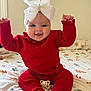 baby, infant, red_clothing, knitted_outfit, white_bow, headband, blue_eyes, smiling, happy, sitting, bed, blanket, holiday_theme, christmas_pattern, pacifier, cute, child, indoors, festive, raising_arms
