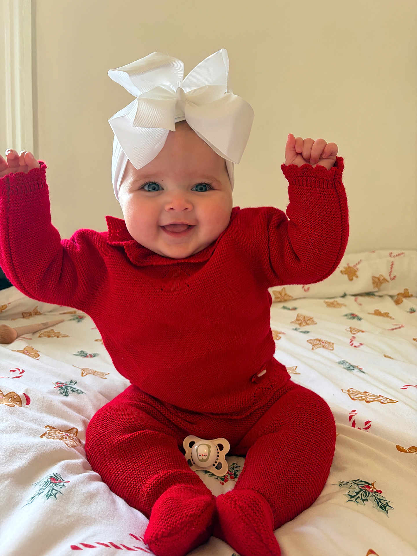Elsie-Mai joined the competition — help win amazing prizes! baby, infant, red_clothing, knitted_outfit, white_bow, headband, blue_eyes, smiling, happy, sitting, bed, blanket, holiday_theme, christmas_pattern, pacifier, cute, child, indoors, festive, raising_arms