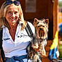 animal, backpack, blond_hair, casual_clothing, cute, daytime, dog, happy, holding, leisure, outdoor, person, pet, portrait, small_dog, smiling, sunglasses, sunlight, woman, yorkshire_terrier
