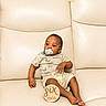 baby, infant, pacifier, couch, leather, milestone, six_months, plaque, clothing, dinosaur_print, child, person, sitting, indoors, cute, young, skin, foot, hand, relaxing