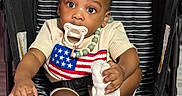 Josiah is registered to the contest to win money with this photo: baby, beaded_necklace, black, child, clothing, cup, curious, cute, expression, graco, indoor, infant, pacifier, person, portrait, seated, sock, striped, stroller, white