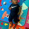 baby, infant, child, playmat, colorful, cartoon, animal, vehicle, fruit, clothing, person, lying_down, looking_away, indoors, cute, blue, orange, red, floor, fun