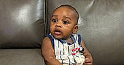 Josiah is registered to the contest to win money with this photo: baby, child, infant, couch, leather, furniture, sitting, striped_clothing, toy, holding, curious, indoor, young_child, portrait, person, home, casual, cute, expression, relaxed