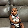 baby, child, infant, couch, leather, furniture, sitting, striped_clothing, toy, holding, curious, indoor, young_child, portrait, person, home, casual, cute, expression, relaxed
