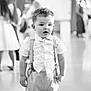 toddler, boy, child, suspenders, shorts, shirt, indoor, black_and_white, portrait, curious, standing, young, people, blurry_background, casual_clothing, expression, cute, person, fashion, event