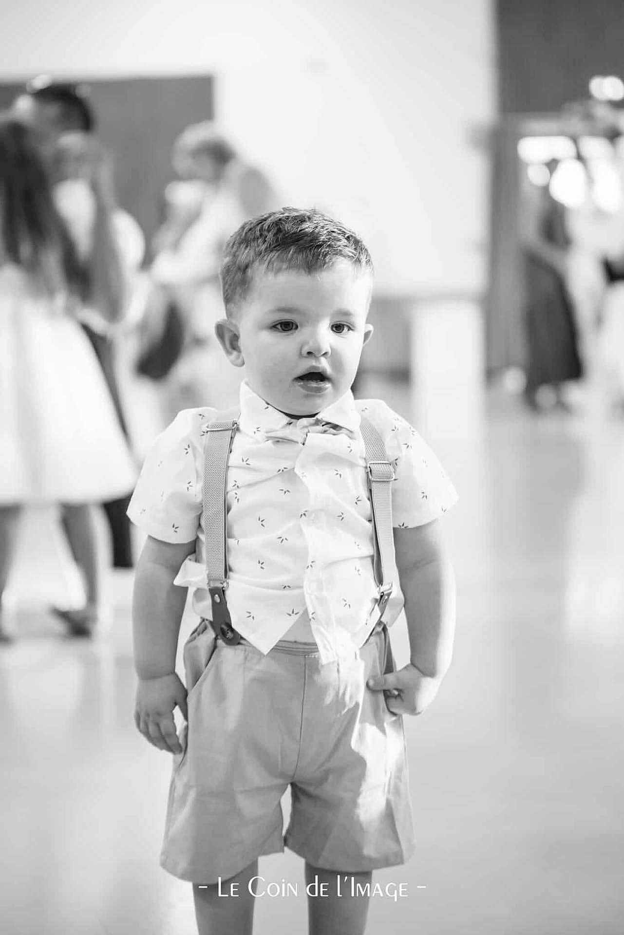 Mayron a rejoint le concours — aidez-le/la à gagner de superbes lots ! toddler, boy, child, suspenders, shorts, shirt, indoor, black_and_white, portrait, curious, standing, young, people, blurry_background, casual_clothing, expression, cute, person, fashion, event