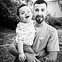 child, toddler, man, tattoo, smile, outdoor, black_and_white, happy, holding, person, casual_clothing, short_hair, beard, nature, grass, footwear, tree, portrait, family, love