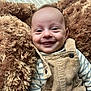 baby, smiling, face, infant, blanket, corduroy, overalls, striped_shirt, happy, cute, child, portrait, closeup, soft_texture, warm_colors, cozy, indoors, person, newborn, expressive