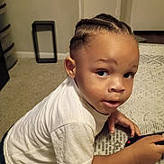 Keondrae is registered to the contest to win money with this photo: toddler, child, cornrows, white_shirt, table, game_controller, indoor, carpet, curious, leaning, person, young_child, casual_clothing, home, portrait, brown_skin, short_sleeves, looking_away, hand, expression