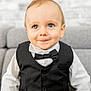 baby, background, black_vest, blue_eyes, bow_tie, boy, child, couch, cute, face, fashion, formal_wear, happy, indoor, portrait, seated, short_hair, smile, toddler, white_shirt