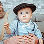 baby, infant, child, blue_eyes, bow_tie, suspenders, flat_cap, hat, adult_hands, wedding_ring, couch, brick_wall, portrait, closeup, indoor, sitting, curious_expression, vintage_style, light_blue_shirt, family_moment