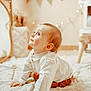 baby, banner, brown_pants, child, cozy, crawling, curious, cute, decor, fairy_lights, floor, home, indoor, infant, portrait, rug, soft_lighting, striped_shirt, texture, warm_tones