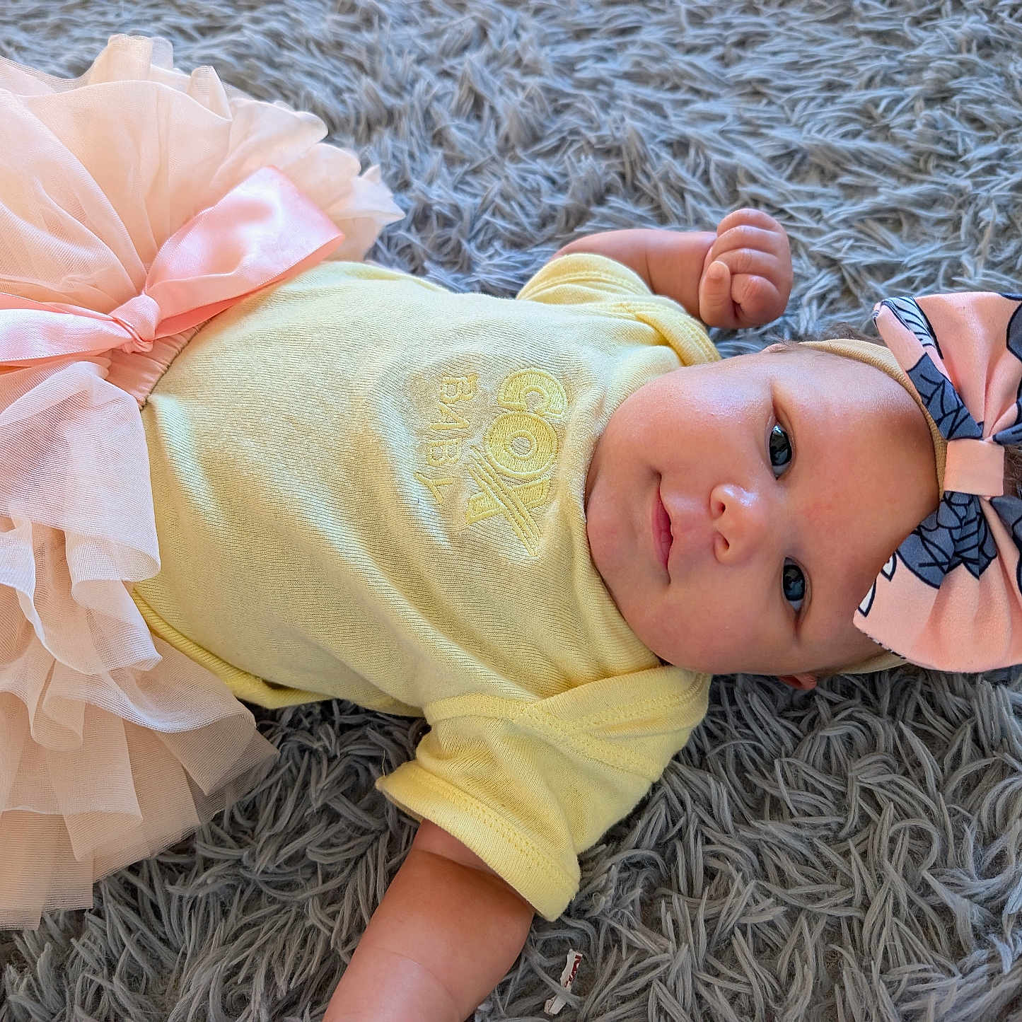 Patience joined the competition — help win amazing prizes! adorable, baby, baby_fashion, bow, child, clothing, cute, face, fluffy_rug, gray_rug, headband, indoor, infant, lying_down, pink, portrait, smiling, soft_texture, tutu, yellow_onesie
