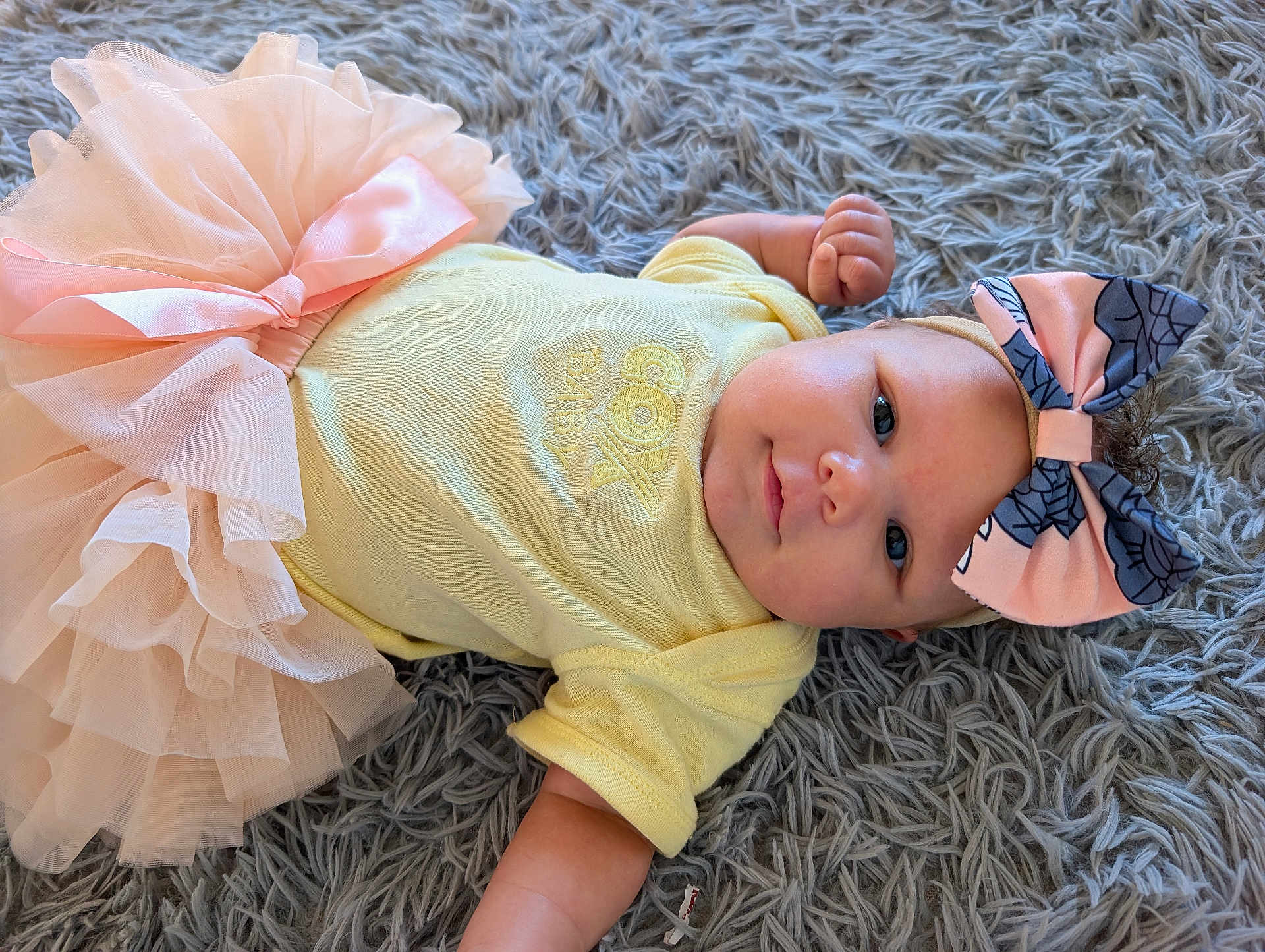 Patience joined the competition — help win amazing prizes! baby, infant, tutu, headband, bow, yellow_onesie, pink, fluffy_rug, gray_rug, lying_down, cute, smiling, child, portrait, soft_texture, clothing, baby_fashion, indoor, adorable, face