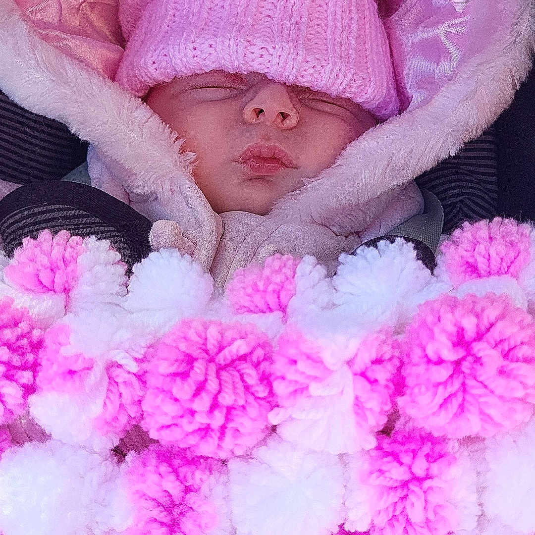 Andie is registered to the contest to win money with this photo: baby, blanket, bundle, car_seat, child, close_up, cozy, cute, face, hood, infant, knitwear, pink_hat, pom_poms, resting, sleeping, soft_texture, warm, winter_clothing, wrapped