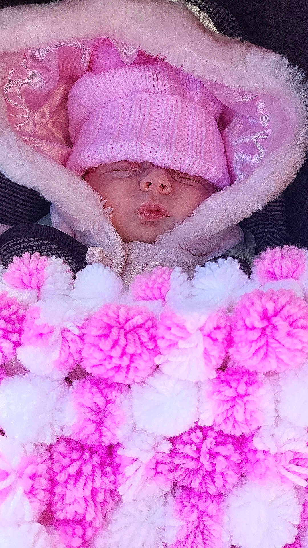 Andie is registered to the contest to win money with this photo: baby, sleeping, pink_hat, blanket, pom_poms, cozy, winter_clothing, hood, child, cute, soft_texture, knitwear, bundle, wrapped, warm, infant, face, close_up, resting, car_seat