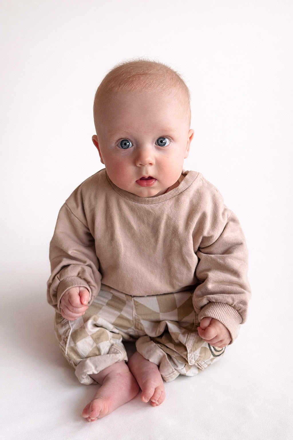Oliver joined the competition — help win amazing prizes! baby, child, infant, blue_eyes, beige_clothing, checkered_pants, sitting, barefoot, cute, portrait, indoors, soft_lighting, curious_expression, small_hands, round_face, casual_wear, studio_shot, minimalist_background, young, person