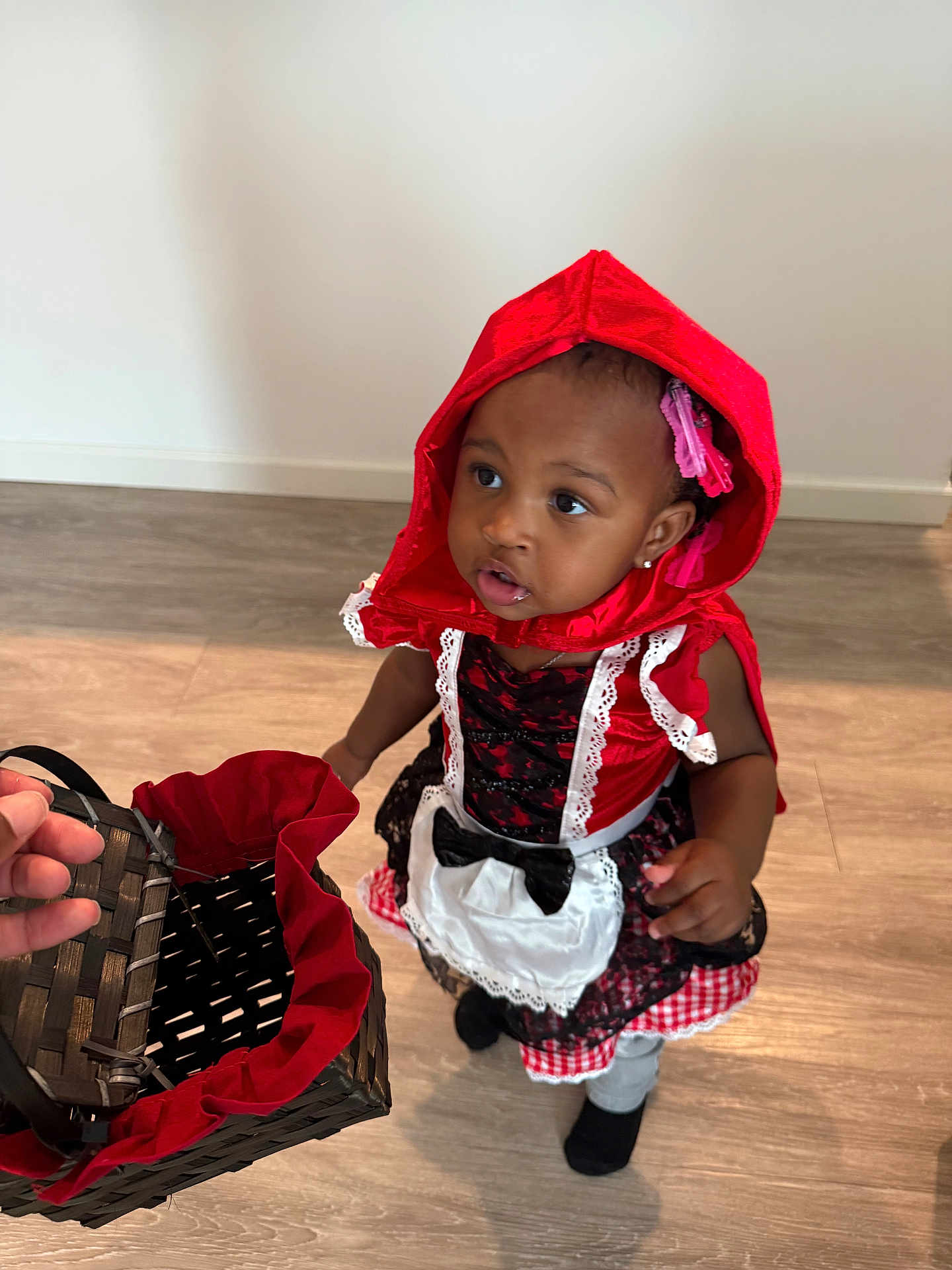 Kamya joined the competition — help win amazing prizes! toddler, child, costume, red_hood, basket, indoor, floor, curious, portrait, black_socks, lace, dress, hand, person, looking_up, girl, hair_clips, playful, young_child, bright_colors
